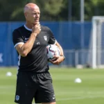 Een KRC Genk-coach observeert een training met een bal in de hand.