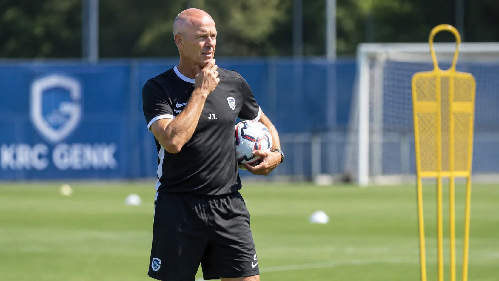 Een KRC Genk-coach observeert een training met een bal in de hand.