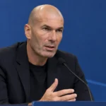 Zinedine Zidane tijdens een persmoment voor een blauwe Franse media-achterwand.