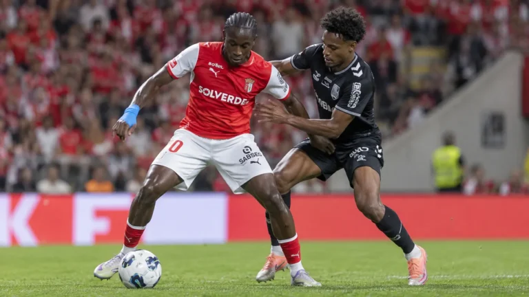 Twee voetballers in rode en zwarte wedstrijdkleding strijden om balbezit.