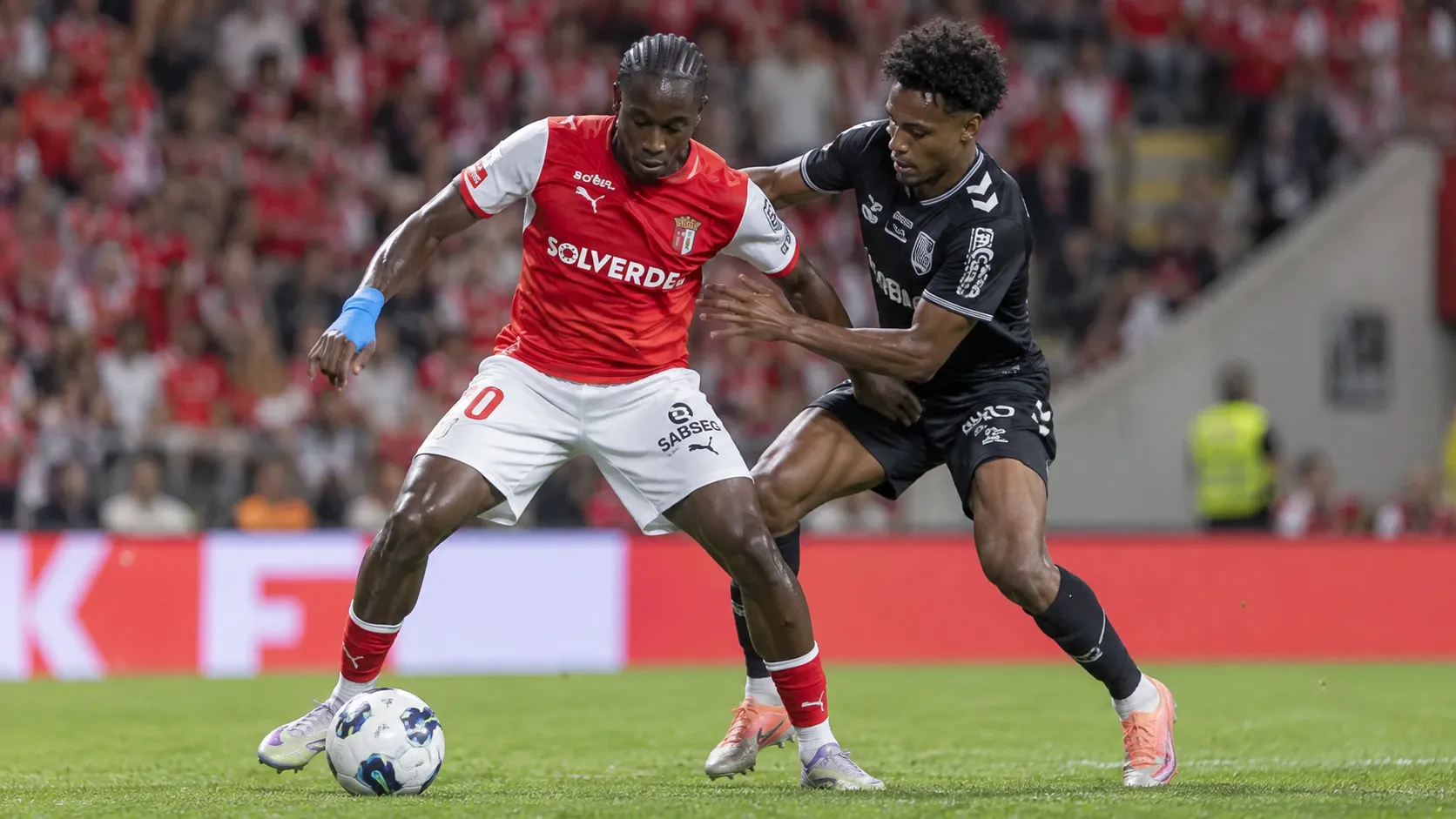 Twee voetballers in rode en zwarte wedstrijdkleding strijden om balbezit.