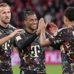 Drie voetballers in donkere shirts begroeten elkaar tijdens een wedstrijd.