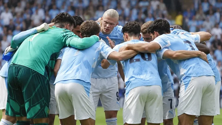 Een groep voetballers in lichtblauwe tenues vormt vlak voor een wedstrijd een kring.