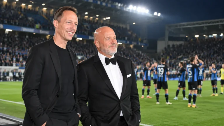 Twee clubvertegenwoordigers op het veld met spelers in blauw-zwarte shirts op de achtergrond.