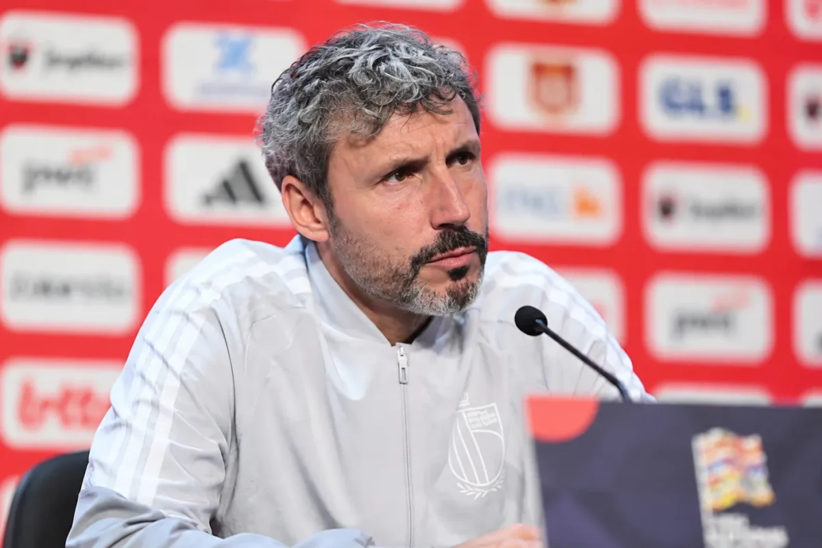 Mark van Bommel luistert aandachtig achter een microfoon op een persconferentie van de Rode Duivels.
