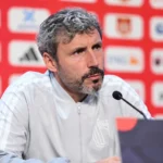Mark van Bommel luistert aandachtig achter een microfoon op een persconferentie van de Rode Duivels.