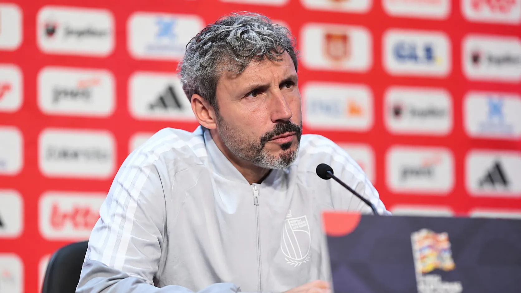 Mark van Bommel luistert aandachtig achter een microfoon op een persconferentie van de Rode Duivels.