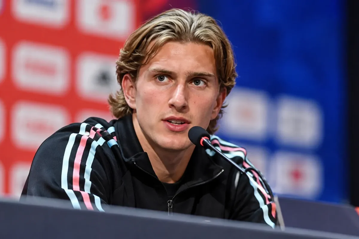Mika Godts tijdens een persconferentie in een donkere trainingsjas.