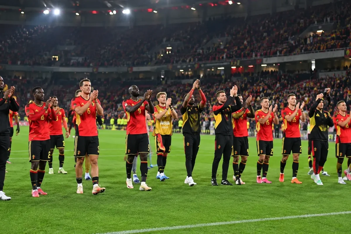 Belgische nationale ploegspelers applaudisseren voor supporters in een verlicht stadion.