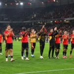 Belgische nationale ploegspelers applaudisseren voor supporters in een verlicht stadion.