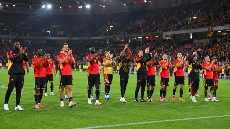 Belgische nationale ploegspelers applaudisseren voor supporters in een verlicht stadion.