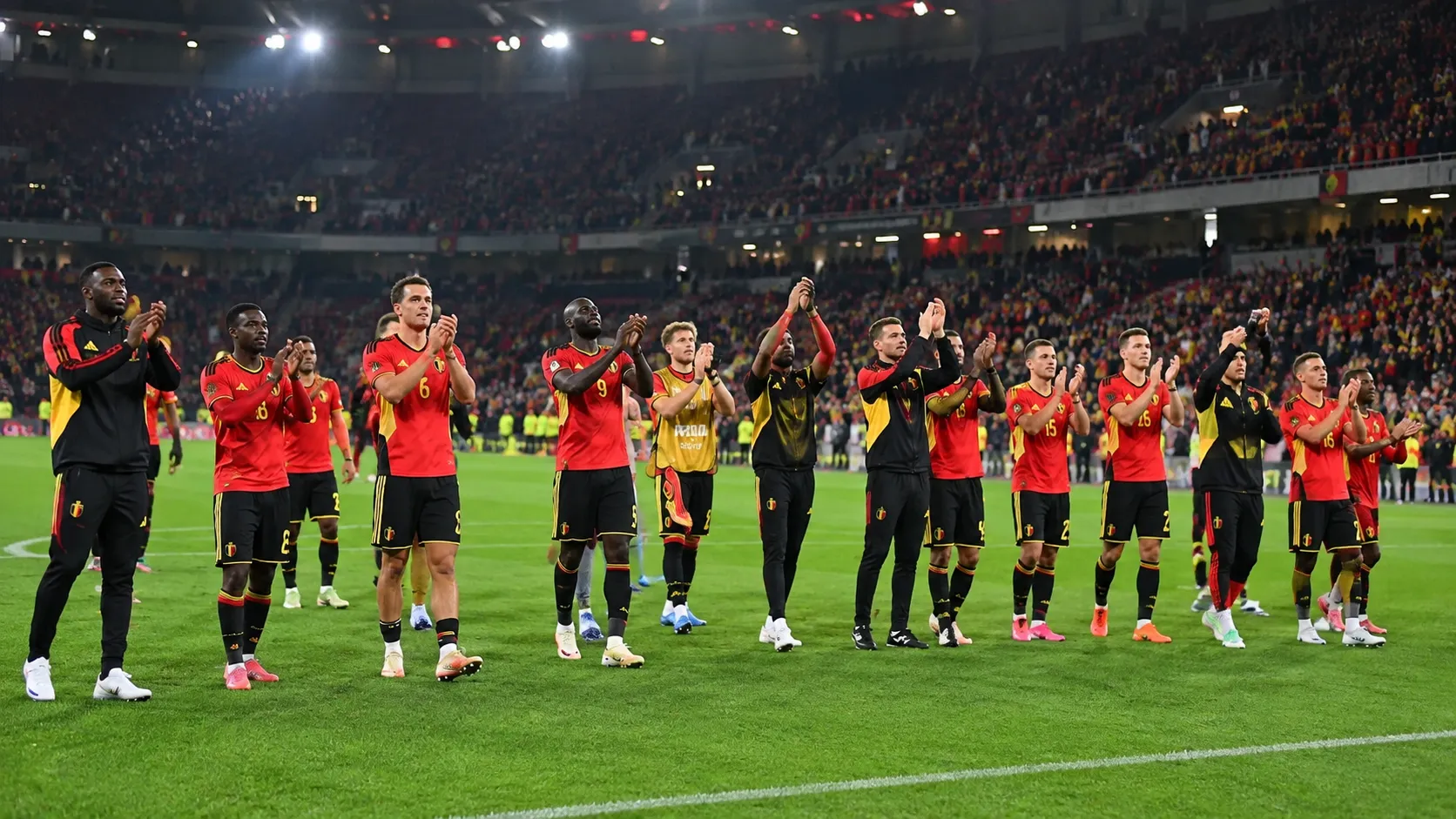 Belgische nationale ploegspelers applaudisseren voor supporters in een verlicht stadion.