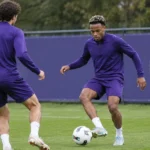 Twee Anderlecht-verdedigers trainen samen op een oefenveld naast een clubbord.