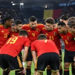 Een groep Belgische internationals in rode nationale tenues verzamelt zich op het veld voor een wedstrijd.