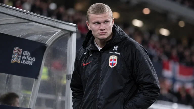 Erling Haaland staat na zijn wissel langs de zijlijn in een Noorse jas.