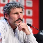 Mark van Bommel luistert aandachtig aan een microfoon tijdens een persmoment.