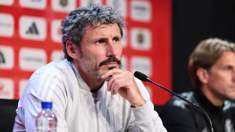 Mark van Bommel luistert aandachtig aan een microfoon tijdens een persmoment.