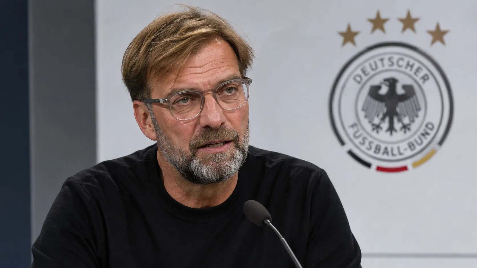 Jürgen Klopp spreekt in een interviewzone met een Duits nationaal ploegembleem op de achtergrond.