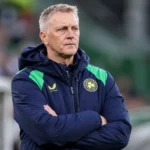 Heimir Hallgrímsson in Ierse trainingsjas aan de zijlijn van een voetbalveld.