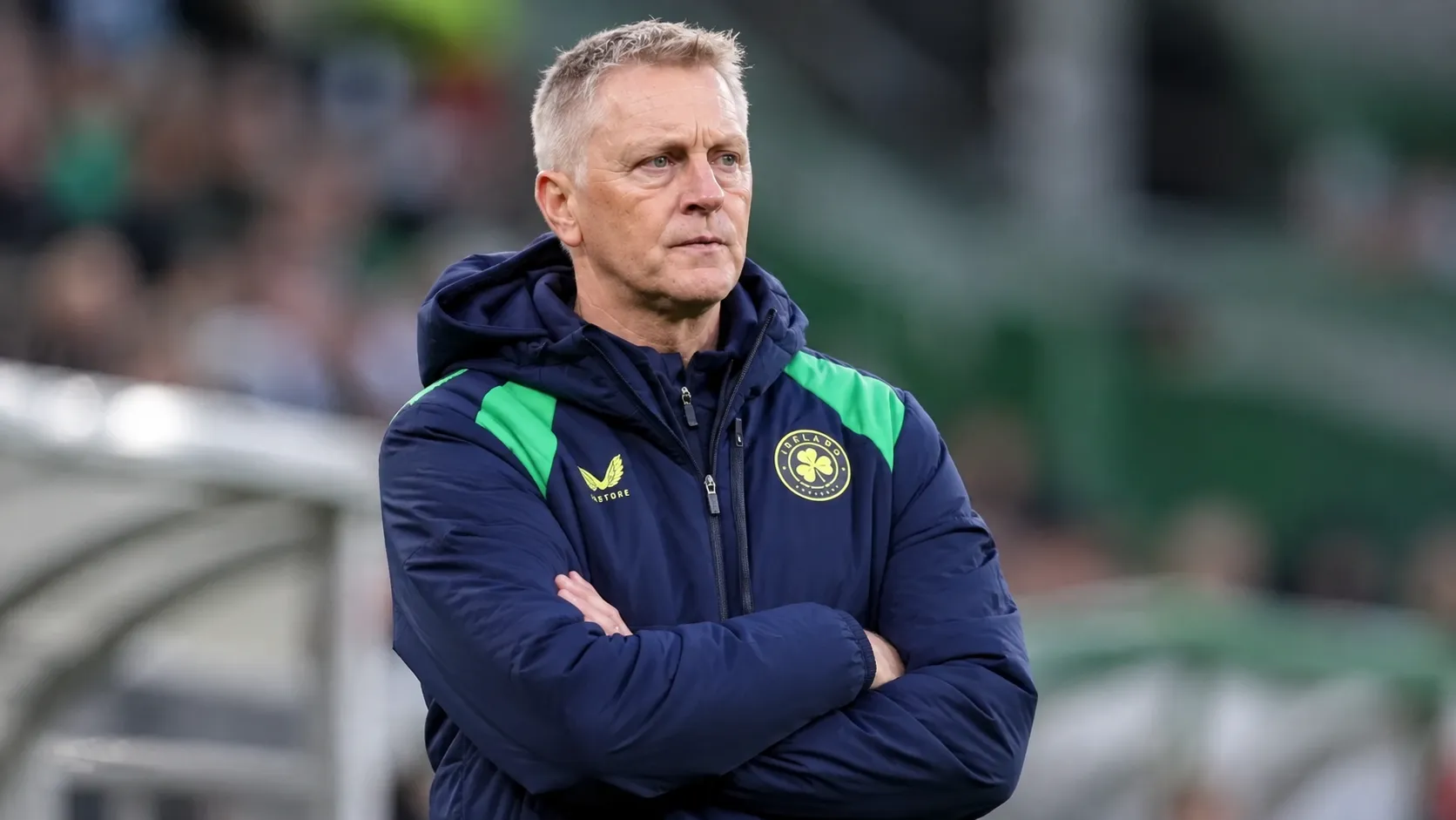 Heimir Hallgrímsson in Ierse trainingsjas aan de zijlijn van een voetbalveld.