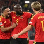 Drie Rode Duivels in rode tenues vieren samen op het veld.