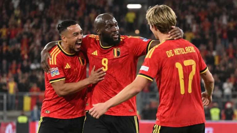 Drie Rode Duivels in rode tenues vieren samen op het veld.