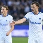 Twee KRC Genk-spelers in witte shirts met blauwe details op het veld.