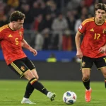 Twee Belgische internationals in rood wedstrijdtenue tijdens een passmoment op het veld.