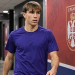 Mihajlo Cvetković in neutrale sportkleding naast een Servisch voetbalembleem in de mixed zone.