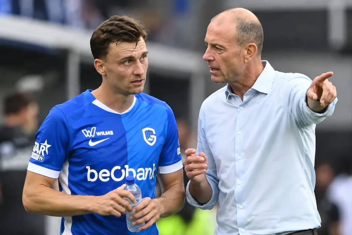Een speler in blauw tenue en een coach overleggen naast het veld.
