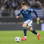 Een jonge voetballer in een blauw tenue tijdens een wedstrijd op een grasveld.