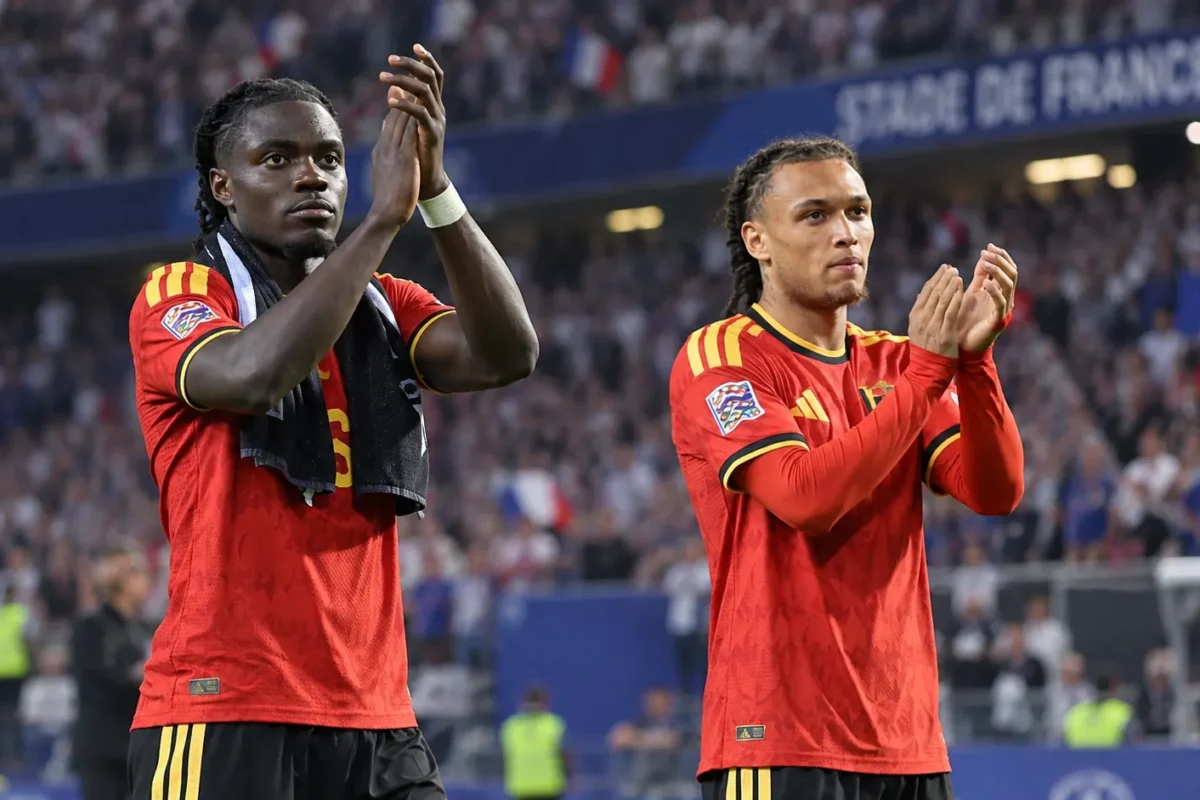 Twee Belgische internationals in rood tenue applaudisseren langs het veld.