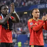 Twee Belgische internationals in rood tenue applaudisseren langs het veld.