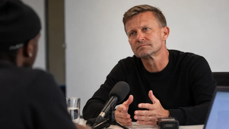 Jesse Marsch tijdens een interview aan een tafel in een rustige binnenruimte.
