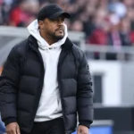 Een coach uit de technische staf langs de zijlijn van een voetbalstadion.