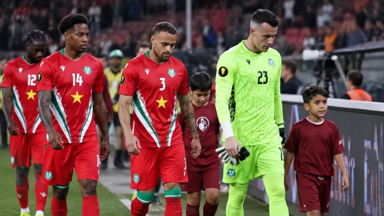 Een groep Surinaamse spelers in rode wedstrijdkleding loopt na de wedstrijd langs de zijlijn.