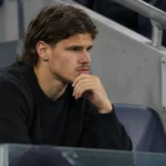 Milos Kerkez in neutrale kleding op de tribune bij een wedstrijd van FK TSC.