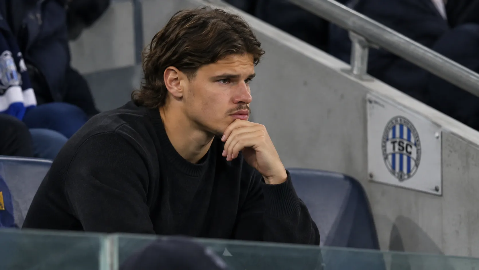 Milos Kerkez in neutrale kleding op de tribune bij een wedstrijd van FK TSC.
