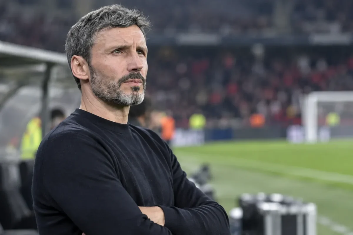 Een niet-geïdentificeerde coach staat geconcentreerd langs de zijlijn van een voetbalveld.