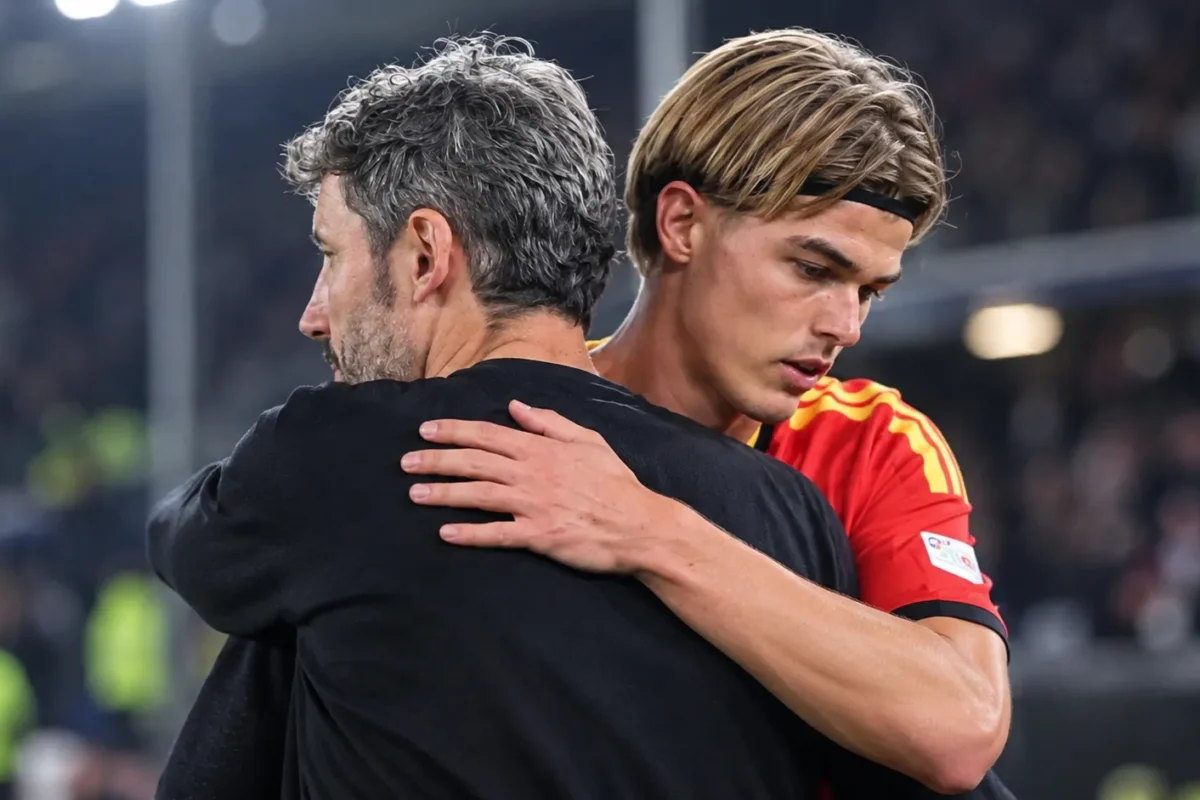 Een coach en een speler in nationaal tenue omhelzen elkaar na een wedstrijd.