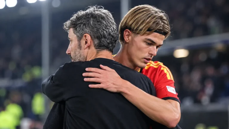 Een coach en een speler in nationaal tenue omhelzen elkaar na een wedstrijd.