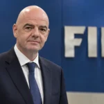 Gianni Infantino in een formele FIFA-conferentieomgeving met een FIFA-embleem op de achterwand.