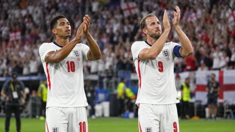 Twee Engelse voetballers in witte shirts applaudisseren richting de tribunes na een wedstrijd.