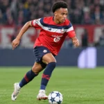 Ethan Mbappé in een rood, wit en donkerblauw wedstrijdshirt terwijl hij met de bal over het veld versnelt.
