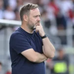 Michael Beale staat nadenkend langs de zijlijn van een voetbalstadion.