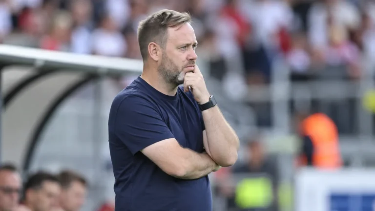 Michael Beale staat nadenkend langs de zijlijn van een voetbalstadion.