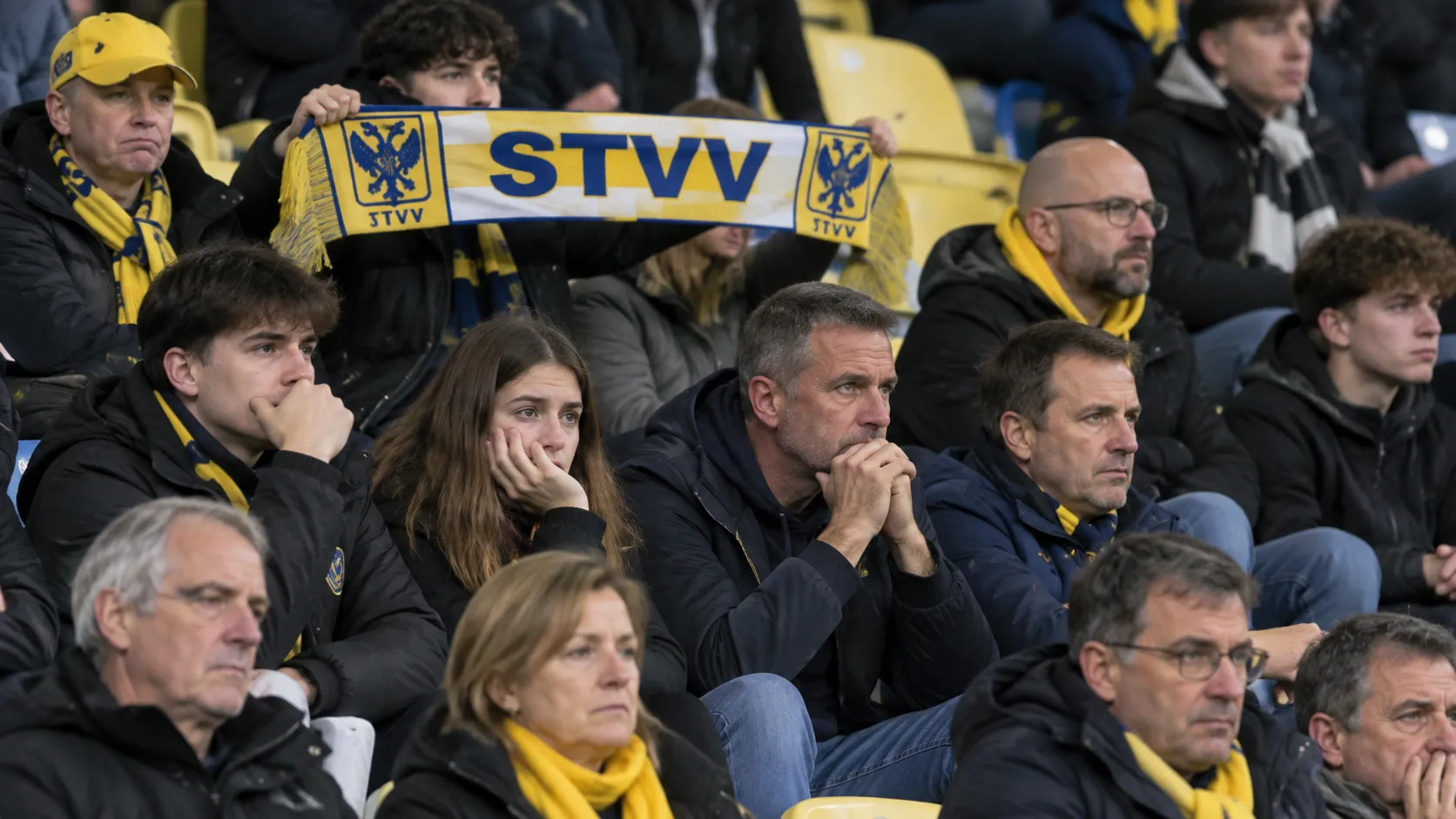 Een groep STVV-supporters in de tribune met een blauw-geel-witte sjaal.