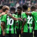 Een groep voetballers in groen-zwarte shirts vormt een kring op het veld.