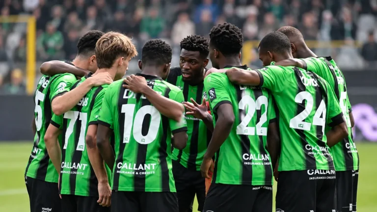 Een groep voetballers in groen-zwarte shirts vormt een kring op het veld.