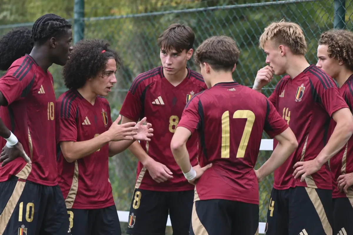 Een groep jonge voetballers in donkerrode Belgische tenues staat samen langs het veld.